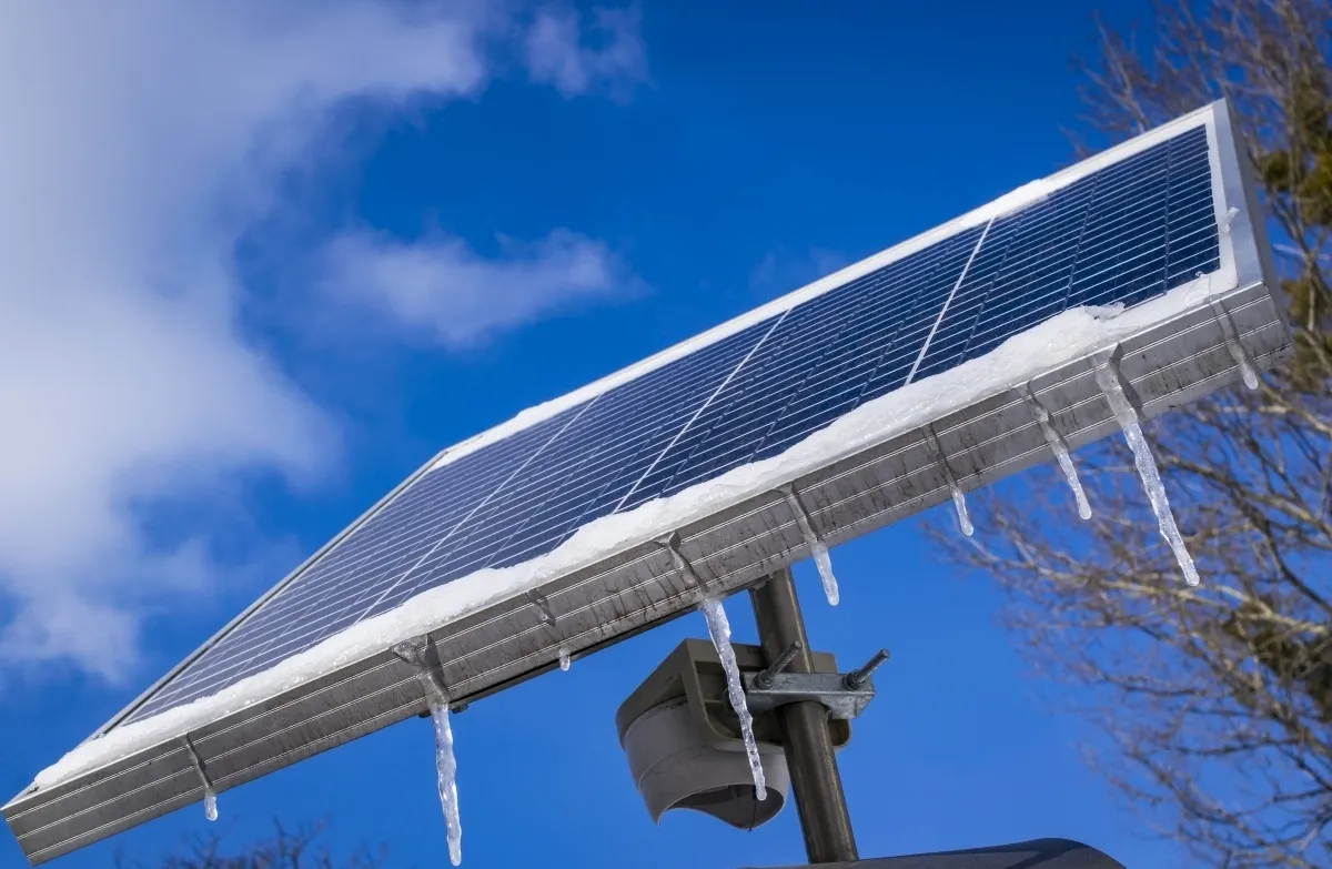 Solar panel edged with snow and hanging icicles against a blue sky
